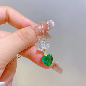 Detail of gold floral necklace with a green heart-shaped stone and sparkling accents