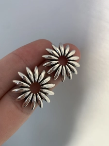 Close-up of vintage hollow silver sunflower stud earrings held in hand for scale