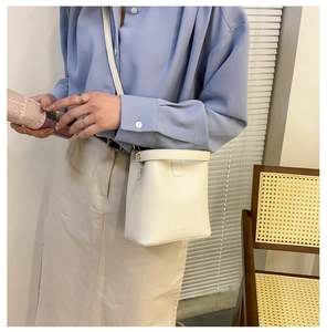 Detailansicht einer weißen Eimer-Tasche aus Leder mit modischem Schriftzug und Gurt