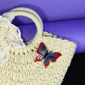 Red butterfly acrylic brooch with blue grey texture and rhinestones on a woven straw bag
