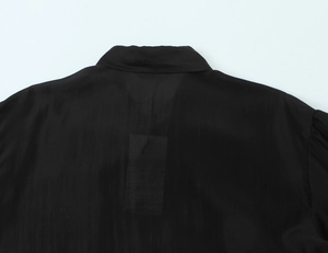 Detail view of lightweight black blouse featuring sheer fabric texture and neckline finish
