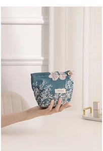 Close-up of a hand holding a portable teal jacquard floral makeup bag with elegant design.