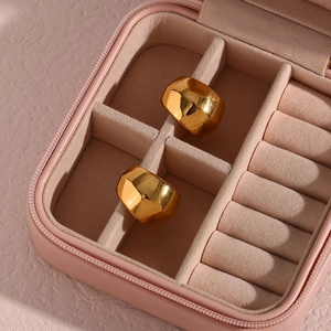 Gros plan de créoles dorées à facettes géométriques dans un écrin à bijoux rose