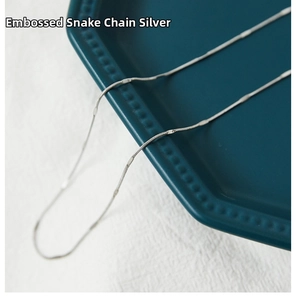 Close-up of polished silver embossed snake bone chain on a ceramic tray backdrop