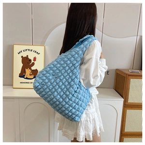 Detail of blue large shoulder bag with bubble texture shown on model in a cozy room
