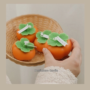 Detail of handmade persimmon-shaped orange candles in a round woven bamboo basket
