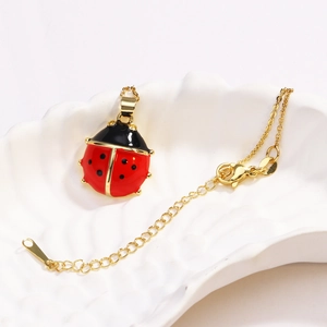 Golden necklace with a red and black ladybug pendant on a white shell ceramic plate