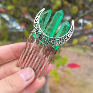 Close-up of a silver moon hair comb featuring raw green crystal pillars and metal filigree