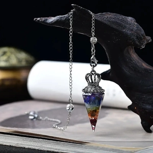 Macro shot of 7 chakra resin hexagonal pendulum with natural stones on wooden branch