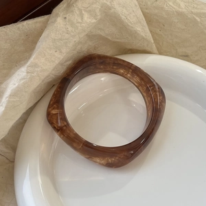 Macro shot of brown tortoiseshell resin bangle with sand texture on a ceramic dish