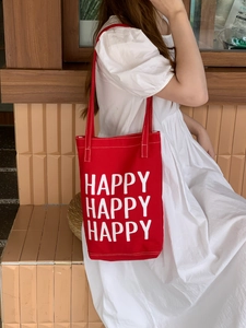 Detailed view of red canvas tote bag with Happy lettering worn with white dress