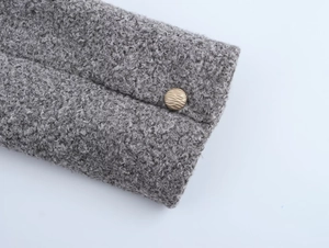Détail du tissu sherpa gris avec un bouton en métal doré texturé sur une veste chic