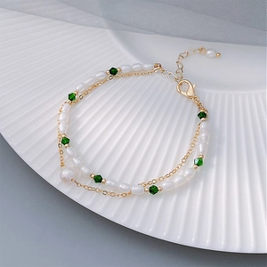Detail of gold double-layer chain bracelet with white pearls and green crystal beads