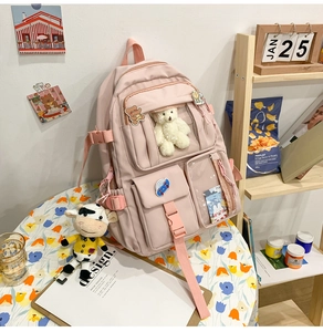 Dettaglio di uno zaino rosa multi-tasche con ciondolo a forma di orso in ambiente accogliente