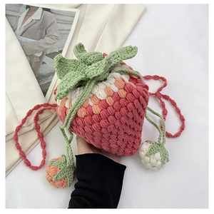 Close-up of handmade crochet strawberry bucket bag with green leaf top and beaded charms