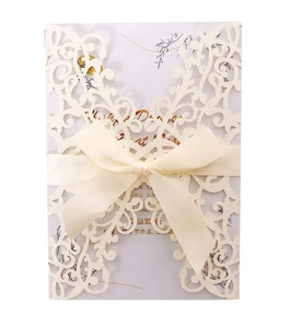 Detail of laser-cut ivory invitation card featuring a glitter finish and satin ribbon bow