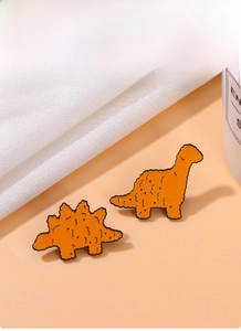 Dettaglio di spille in smalto a forma di dinosauro arancione con trama stile pollo fritto