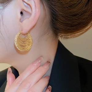 Close-up of elegant gold twisted layered chain hoop earrings worn by a female model