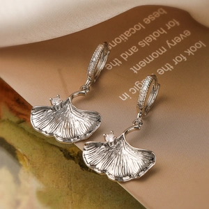 Macro shot of silver ginkgo leaf earrings with shimmering zircons and silk backdrop