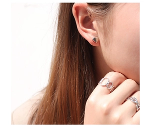 Close-up of a silver heart-shaped stud earring and minimalist rings on a model