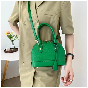 Detail of green shell bag with crocodile texture and gold zipper on a beige blazer