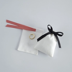Detail of white velvet jewelry pouches with pink and black ribbons and a gold ear cuff