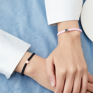 Bracciali di coppia intrecciati a mano in nero e rosa con ciondoli a cuore su sfondo materico