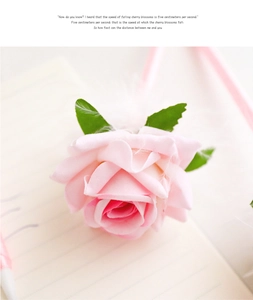 Close-up of a pink rose fabric flower pen with green leaves on a notebook page