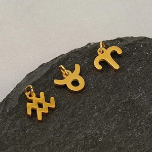 Detailed macro view of three gold hollow-out zodiac pendants on black textured stone