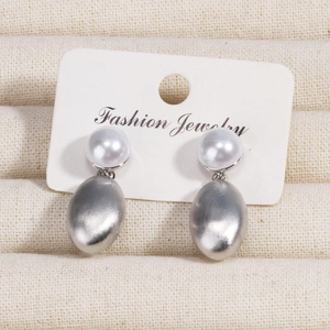 Detailed macro view of pearl stud earrings with brushed silver metal oval drops