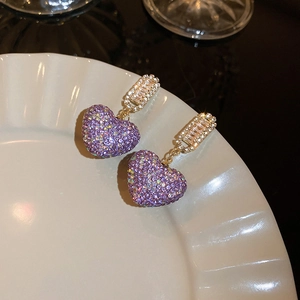 Close-up of heart-shaped purple zircon earrings with gold base on white ceramic tray
