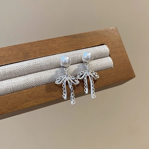 Close-up of pearl bow drop earrings on a wooden stand with elegant silver details