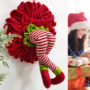 Close-up of red and green knitted elf legs Christmas wreath hanging on a white wall