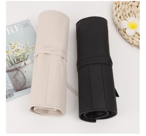 Detail of rolled lychee pattern PU leather brush bags in cream and black with strap closures