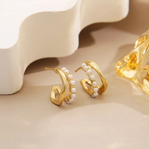 Macro detail of golden C-shaped twisted earrings featuring white pearls and matte finish