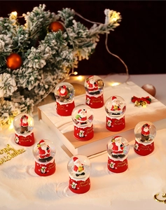 Close-up of Santa Claus snow globe with red base on snow with warm festive lights