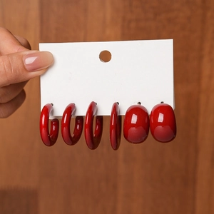 Macro detail of three pairs of red acrylic hoop and oval stud earrings on a display card