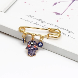 Close-up of golden Hamsa Hand and Evil Eye charms on safety pin brooch detail