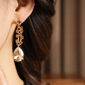 Close-up of champagne gold pear-cut crystal drop earrings worn by a model in soft light