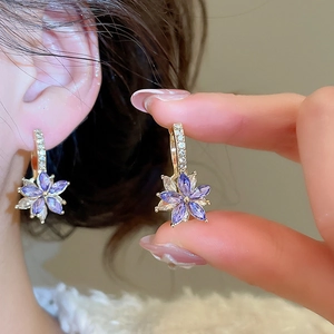 Detailed close-up of gold flower earrings with purple and clear marquise zircons