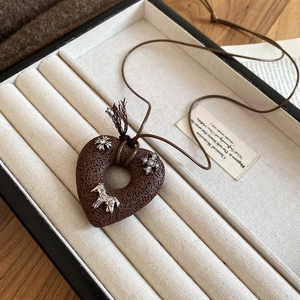 Close-up of a vintage heart pendant with silver charms on a brown woven necklace cord