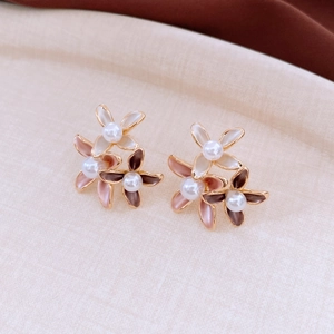 Detail of three-color floral stud earrings with white pearls on a soft textured background