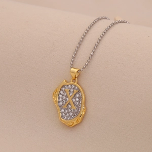 Macro detail of gold-tone necklace featuring an irregular pendant with crystals and letter X