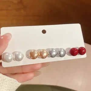 Set of four pairs of elegant round pearl stud earrings in white, gold, grey, and red