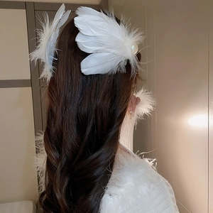 Detail of white feather hair clip with pearl accent worn on long wavy hair