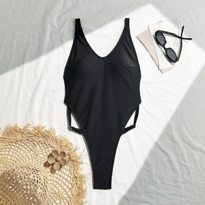 Flat lay of black high-cut one-piece swimsuit with side straps and beach accessories