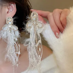 Elegant bow earrings with white feathers, crystals and pearls worn by a model