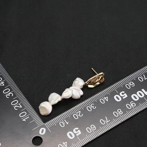 Baroque pearl drop earrings with gold metal accents measured on a scale background