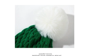 Close-up of green cable-knit Christmas hat featuring a large white faux fur pompom detail