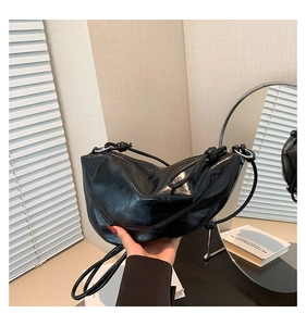 Detail of a black crescent shoulder bag featuring glossy pleated leather and knot strap